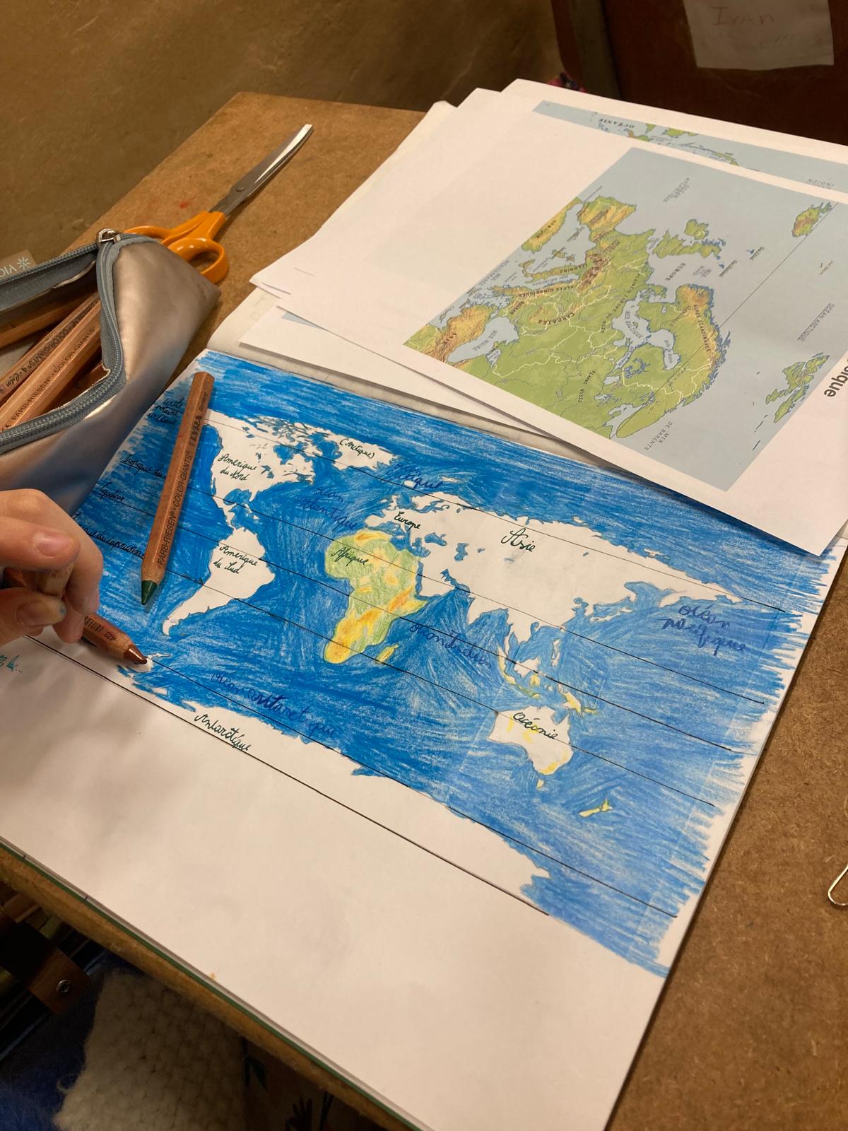Un cahier de 7ᵉ ouvert : la mappemonde dessinée et coloriée à la main